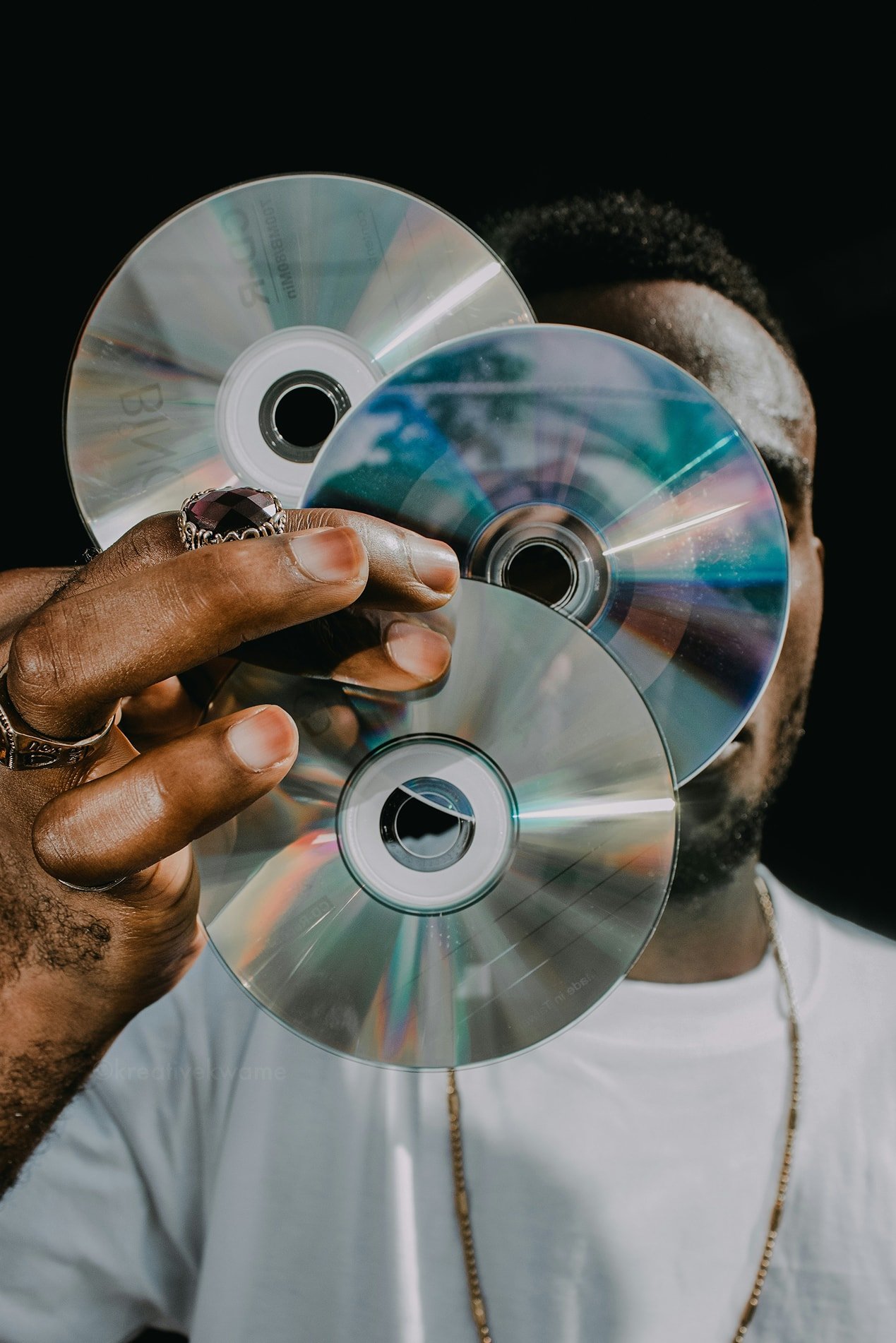 Hand holding three compact discs in front of a face, iridescent surfaces catching the light