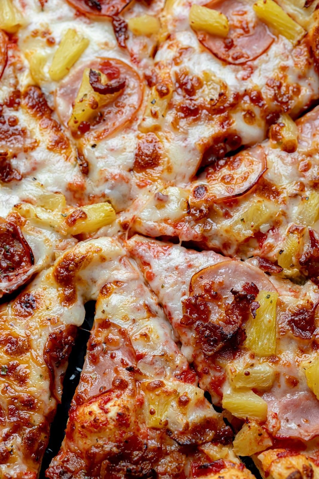 Close-up of a Hawaiian pizza with pineapple, ham, and melted mozzarella